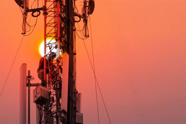 Un ingénieur ou un technicien travaillant sur un pylône de grande hauteur. Il s'agit de travaux en hauteur à risque où le personnel utilise des équipements de sécurité sur la structure.