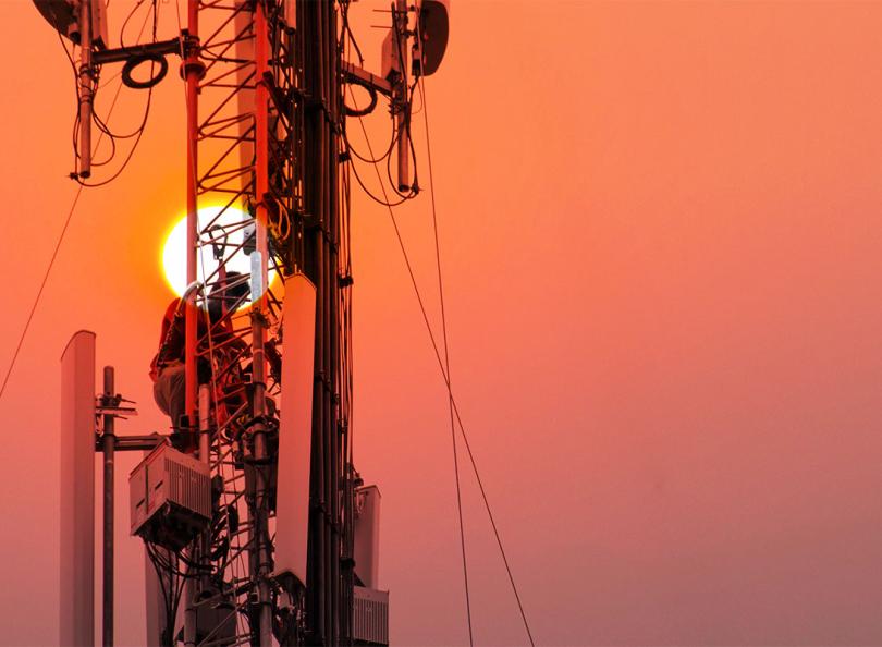 Un ingénieur ou un technicien travaillant sur un pylône de grande hauteur. Il s'agit de travaux en hauteur à risque où le personnel utilise des équipements de sécurité sur la structure.
