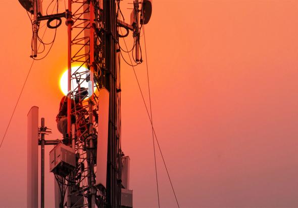 Un ingénieur ou un technicien travaillant sur un pylône de grande hauteur. Il s'agit de travaux en hauteur à risque où le personnel utilise des équipements de sécurité sur la structure.